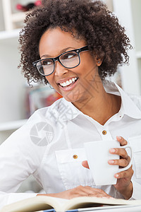 美丽快乐的混血非裔美国女孩轻女子,牙齿完美,戴着眼镜,喝杯咖啡茶,读本书图片