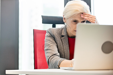 疲惫的成熟女商人办公室的桌子上用笔记本电脑图片