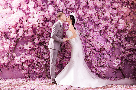 婚礼夫妇亲吻白色的侧视,站墙上,覆盖着粉红色的花图片