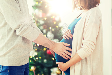 怀孕,寒假人们的接近快乐的男人触摸他怀孕的妻子肚子诞节回家诞节男人孕妇图片