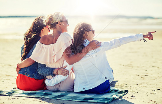 暑假,假期,旅行人们的群微笑的轻女戴着太阳镜,坐沙滩毯子上,指着什么东西群戴太阳镜的微笑女人海滩上图片
