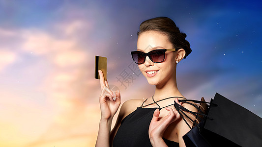 销售,财务,时尚,人奢侈的快乐美丽的轻女人戴着黑色太阳镜,信用卡购物袋天空背景带着信用卡购物袋的快乐女人背景图片
