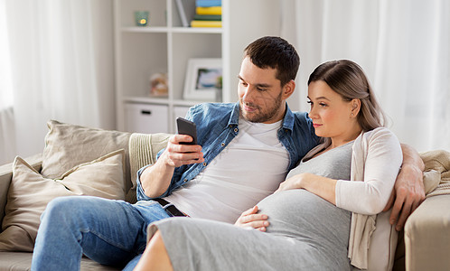智能家怀孕,技术人的快乐的男人他怀孕的妻子家用智能手机家里智能手机的男人怀孕的妻子背景