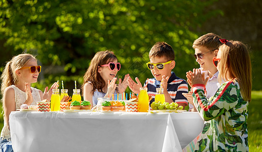 假期,童庆祝快乐的孩子蛋糕上着蜡烛,坐夏天的花园聚会上,为生日男孩鼓掌快乐的孩子夏天的生日聚会上吃蛋糕图片