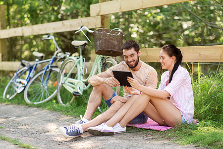 人,技术生活方式的快乐的夫妇与平板电脑电脑自行车夏季公园与平板电脑自行车夏季公园背景图片