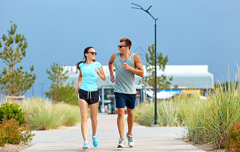 健身,运动生活方式的快乐的夫妇穿着运动服装太阳镜沿着夏季海滩跑步穿着运动服的夫妇海滩上跑步图片