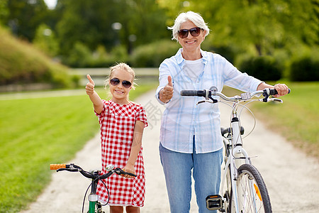 家庭休闲人的快乐的祖母孙女,骑着自行车,夏季公园竖大拇指祖母孙女骑自行车图片