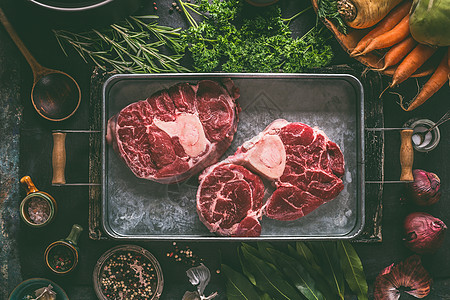 肉骨茶生牛肉腿与骨头肉汤,汤炖金属托盘与美味烹饪的成分根蔬菜,草药香料黑暗的乡村厨房桌子背景,顶部视图背景