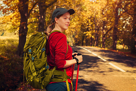 轻的女游客秋天的季节带着棍子背包路上散步图片