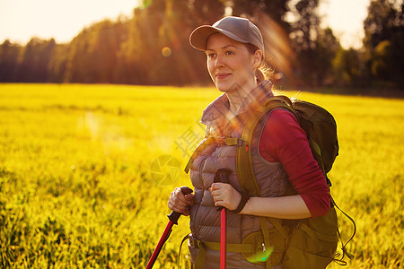 轻的女游客夕阳下用棍子背包绿色的夏季田野上散步图片