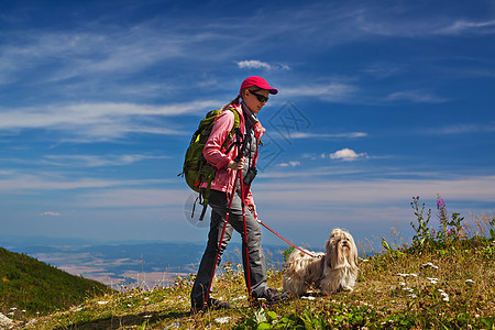 轻的女游客带着狗蓝天背景的山上旅行图片