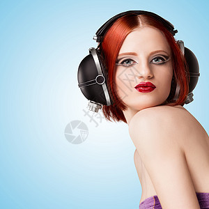 个迷人的感女孩的肖像,戴着老式的音乐耳机,蓝色背景上听音乐图片