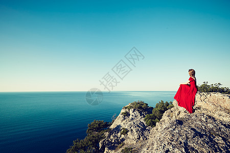 穿着红色连衣裙的轻美女望着山海蓝天背景上的自然女孩时尚照片图片