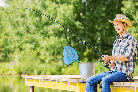 夏天钓鱼戴帽子的轻人坐桥上钓鱼图片