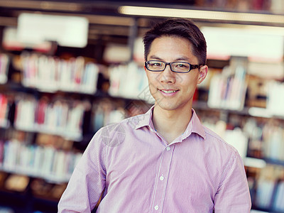 图书馆里快乐的男学生快乐的亚洲男学生戴着眼镜站图书馆图片