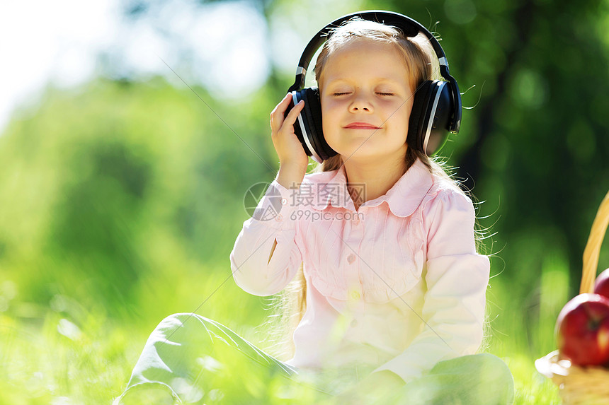 可爱的女孩戴着耳机坐夏天的公园里大自然的声音图片