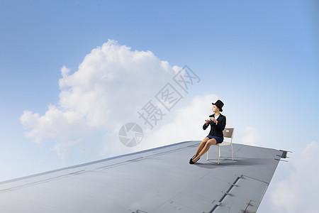 飞行飞机的机翼上轻的女商人坐飞机机翼的边缘图片