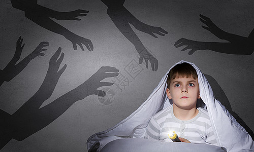 孩子的噩梦带着手电筒躺毯子下的小吓坏了的男孩背景图片