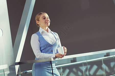 办公楼里魅力的女人轻的金发女人现代璃内部,手里着杯子图片