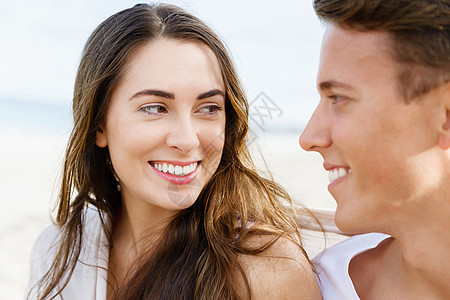 男袜浪漫的轻夫妇坐海滩上浪漫的轻夫妇坐海滩上互相看着背景