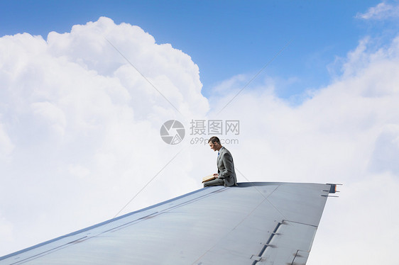 飞行飞机的机翼上轻的商人坐飞机机翼的边缘,手里着书图片