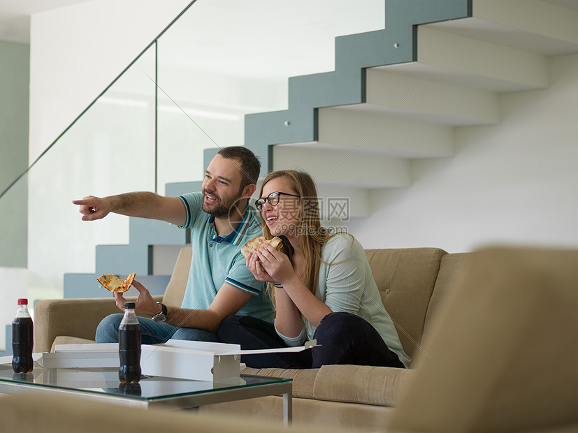 轻英俊的夫妇兴高采烈地花时间他们豪华的别墅里吃比萨饼图片
