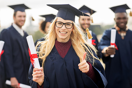 教育毕业手势人的群快乐的国际学生穿着灰浆板学士服,毕业证书竖大拇指图片