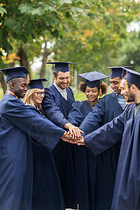 教育毕业人的群快乐的国际学生穿着迫击炮板学士服,把手放图片