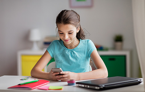 孩子,技术沟通微笑的女孩分散注意力,家庭作业短信智能手机家里智能手机的女孩分散了家庭作业的注意力图片