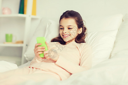 人,孩子,休息技术快乐的微笑女孩躺家里的床上,用智能手机睡着快乐的女孩躺床上,家里智能手机图片