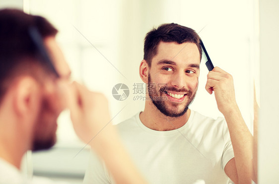 美丽,修饰人的微笑的轻人看着镜子,家里的浴室用梳子梳头快乐的男人浴室用梳子刷头发图片