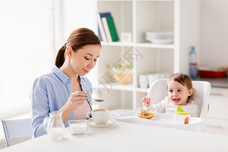 家庭,饮食,早餐人们的快乐的母亲添加糖咖啡杯小婴儿与食物坐高椅子家里厨房快乐的母亲婴儿家里吃早餐图片