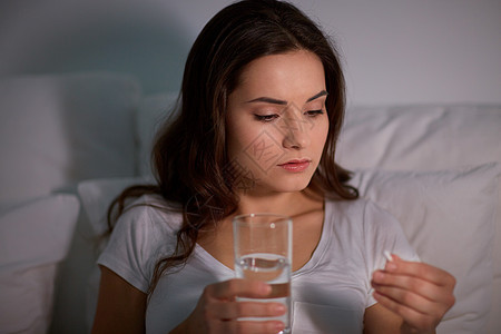 药物,医疗保健人们的妇女晚上的家里床上吃药喝水家里床上药丸水的女人图片