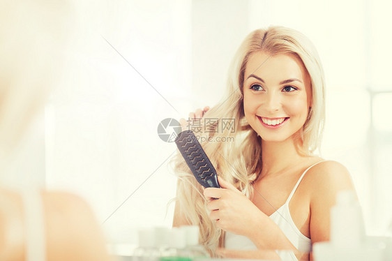 美丽,修饰人的微笑的轻女人看着镜子,家里的浴室用梳子梳头快乐的女人浴室用梳子刷头发图片