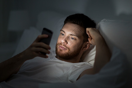 技术互联网通信人的轻人晚上家里的床上用智能手机发短信晚上床上智能手机的轻人图片