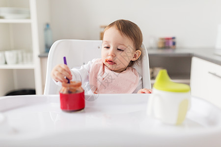 食物,孩子,喂养人的小女婴着勺子坐高椅子上,家里的厨房里吃罐子里的纯净物带勺子的女婴家吃罐子里的泥图片