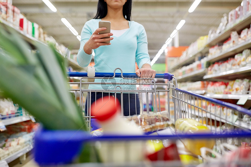 消费主义,技术人的妇女与智能手机,购物车手推车购买食品杂货店超市智能手机的女人超市买食物智能手机的女图片