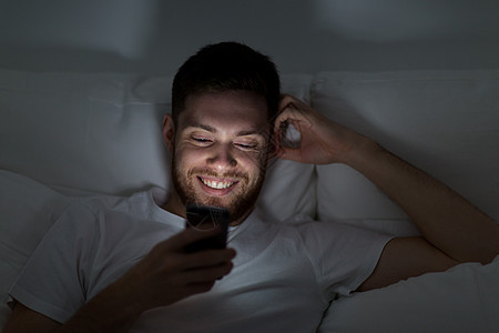 技术,互联网,交流人们的快乐的微笑轻人家里的智能手机上发短信快乐的轻人,晚上床上智能手机图片