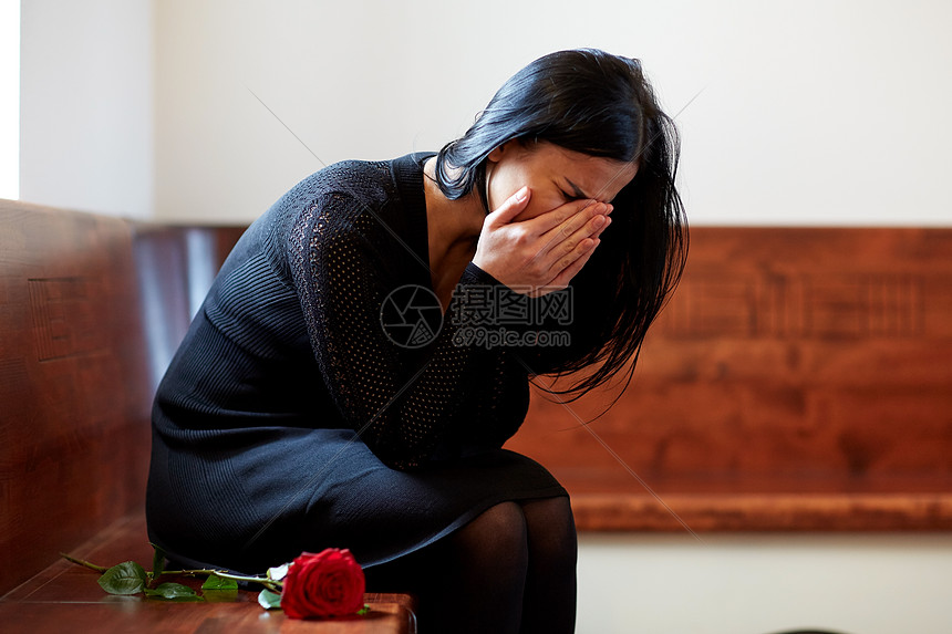人们,悲伤哀悼的哭泣的女人与红玫瑰坐长凳上的葬礼教堂教堂的葬礼上
