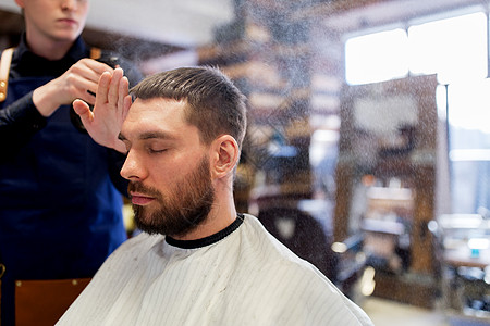 美容,美发人的发型师应用头发造型喷雾水的男客户理发店理发师将造型喷雾应用于男头发图片