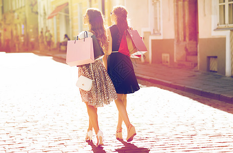 线上购物销售,消费主义人的快乐的轻妇女带着购物袋走城市街道上快乐的女人带着购物袋城市里散步背景
