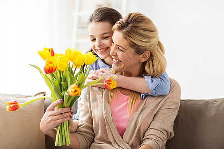 送母亲花的女孩人,家庭假期的快乐的女孩送郁金香花拥抱她的母亲家里快乐的女孩家里给妈妈送花背景