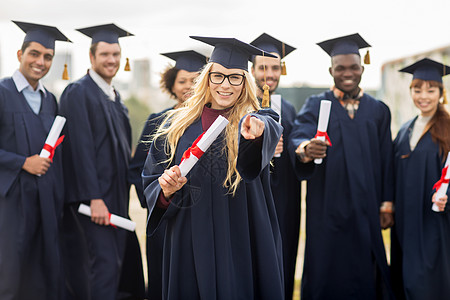 教育毕业人的群快乐的国际学生穿着灰浆板学士服,文凭指向你快乐的学生用文凭指着你图片