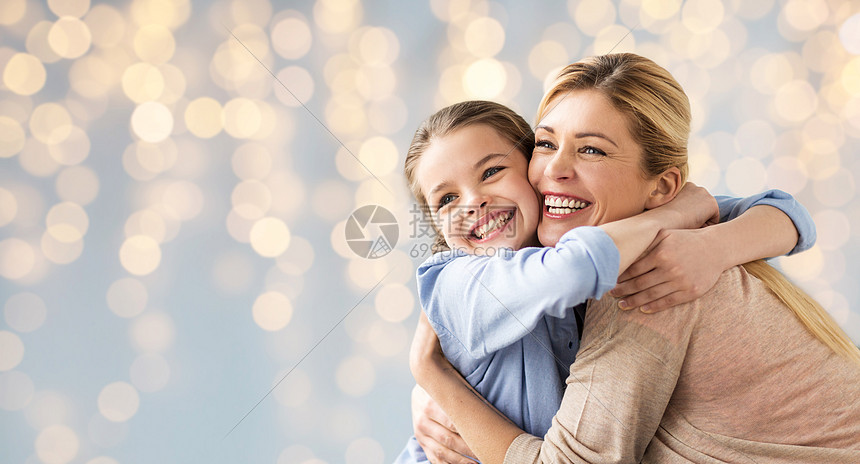 人家庭的快乐的微笑女孩与母亲拥抱节日的灯光背景快乐的女孩母亲拥抱灯光图片