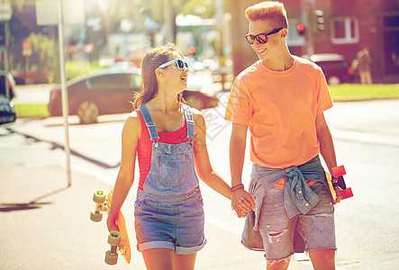 暑假,极限运动人们的快乐的青少夫妇与短现代巡洋舰滑板沿着城市街道行走轻夫妇城市街道上滑板图片