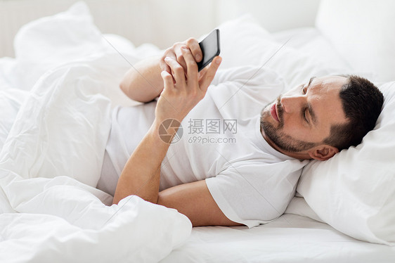技术,互联网,通信人的快乐的轻人智能手机上发短信家里早上床上智能手机的轻人图片
