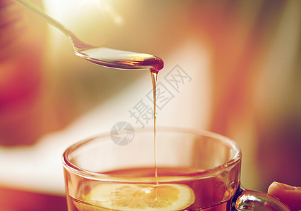健康食品,饮食民族科学的密切妇女添加蜂蜜与柠檬茶杯特写女人用柠檬茶中加入蜂蜜图片
