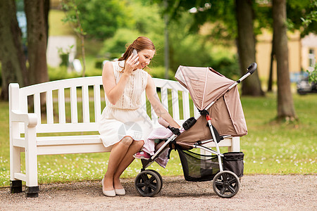 母亲技术人的快乐的母亲婴儿车上的女婴夏季公园打电话智能手机快乐的母亲公园用智能手机婴儿车图片