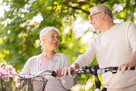 老人,人生活方式的快乐的老夫妇步行与固定自行车夏季城市公园交谈快乐的老夫妇夏季公园骑自行车图片