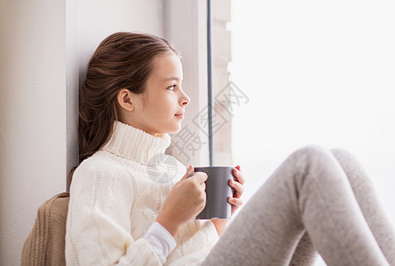 童人们的美丽的女孩与茶杯毛衣坐家里的窗户冬天带着茶杯的女孩坐家里的窗户上图片